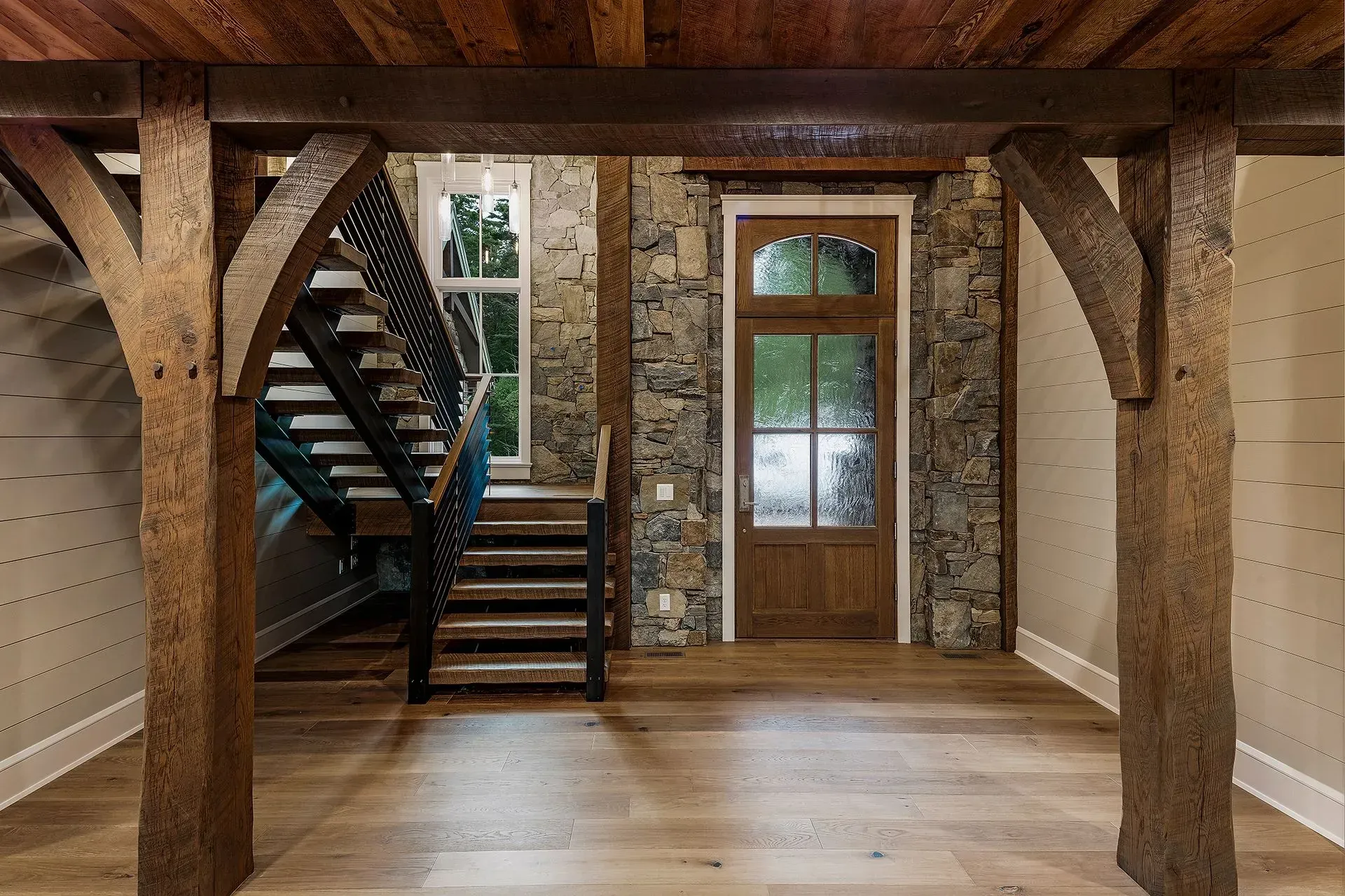 Interior view of a rustic home with wooden beams, stone walls, stairs, and a doorway.