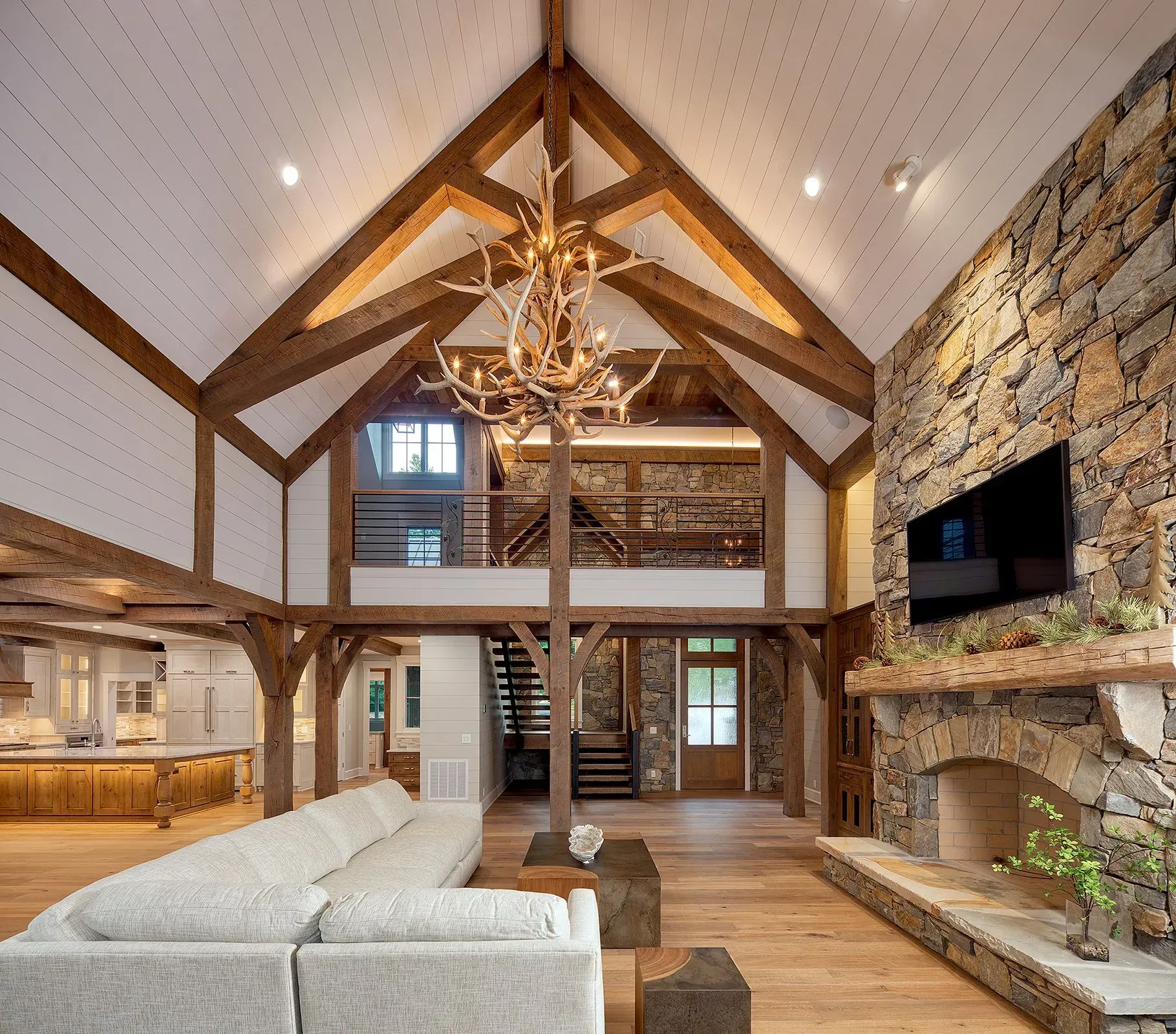 Spacious living room with stone fireplace, wooden beams, and a chandelier. Couch and a loft.