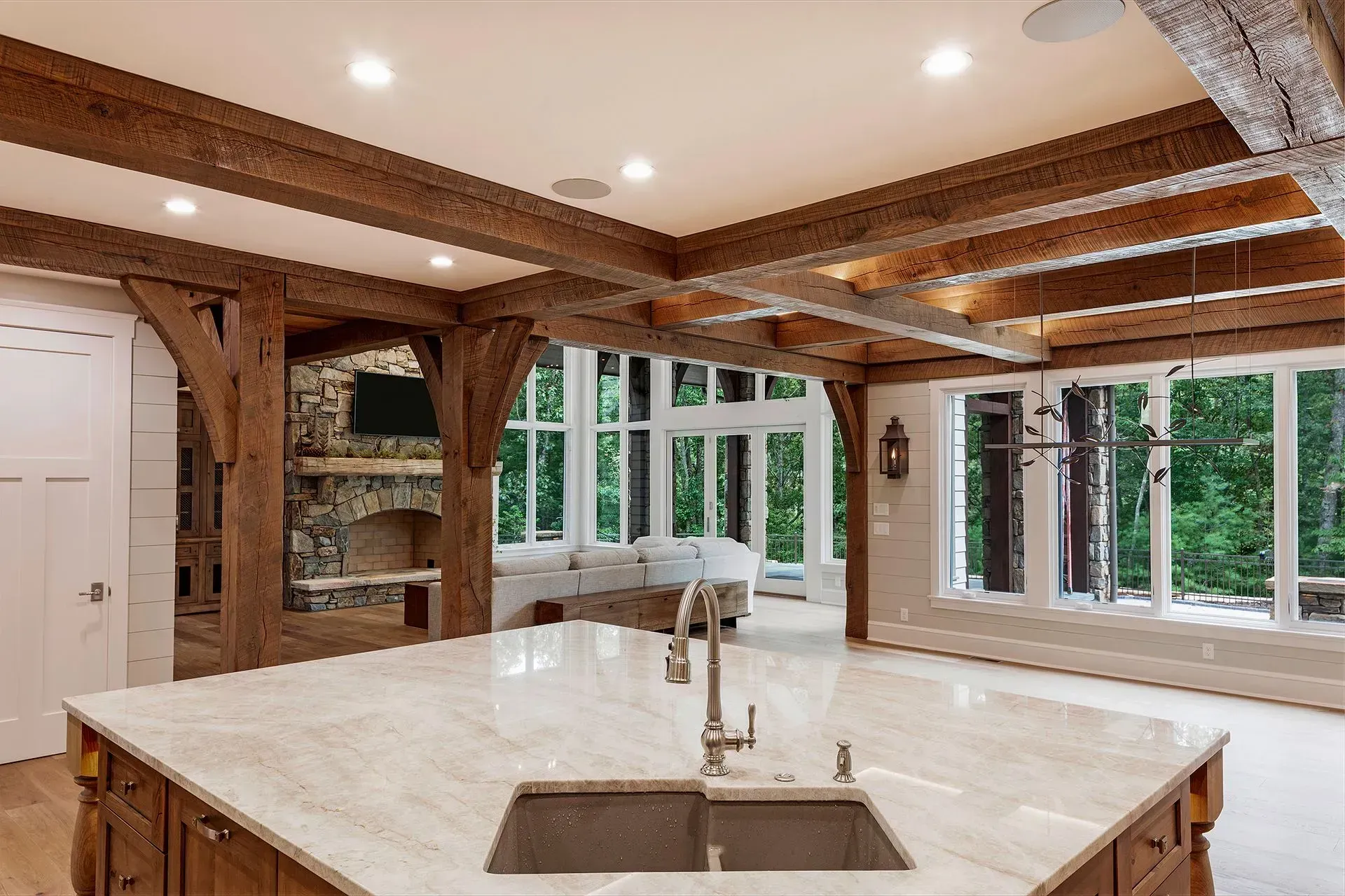 Kitchen with wooden beams, stone fireplace, large windows, and an island with a sink.