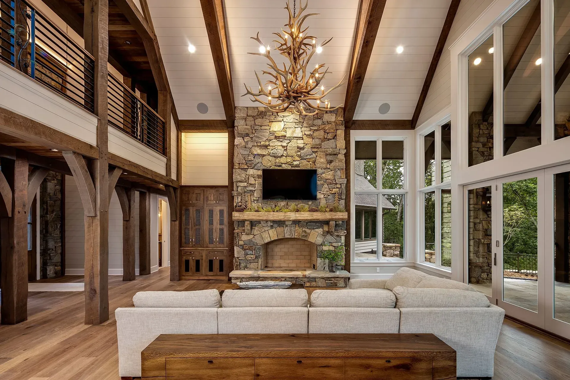 Living room with stone fireplace, large windows, wood beams, and a white sectional sofa.