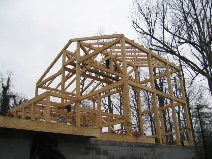 Wooden frame of a house under construction; exposed beams and trusses; outdoors, cloudy sky.