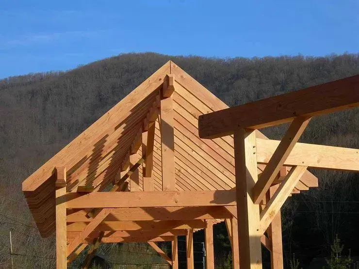 Wooden gazebo under construction with a sloped roof against a mountainous background.