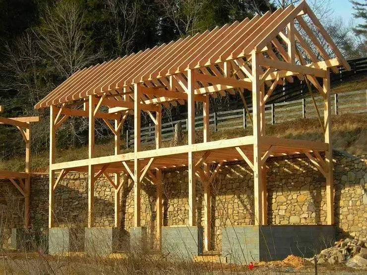 Wooden timber frame building under construction, on concrete footings, outdoors, daylight.