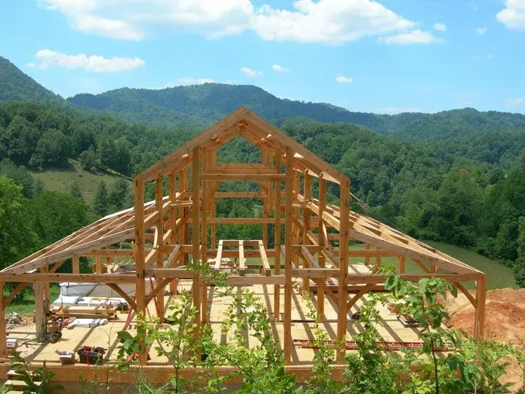 Wooden barn frame under construction with mountain backdrop.