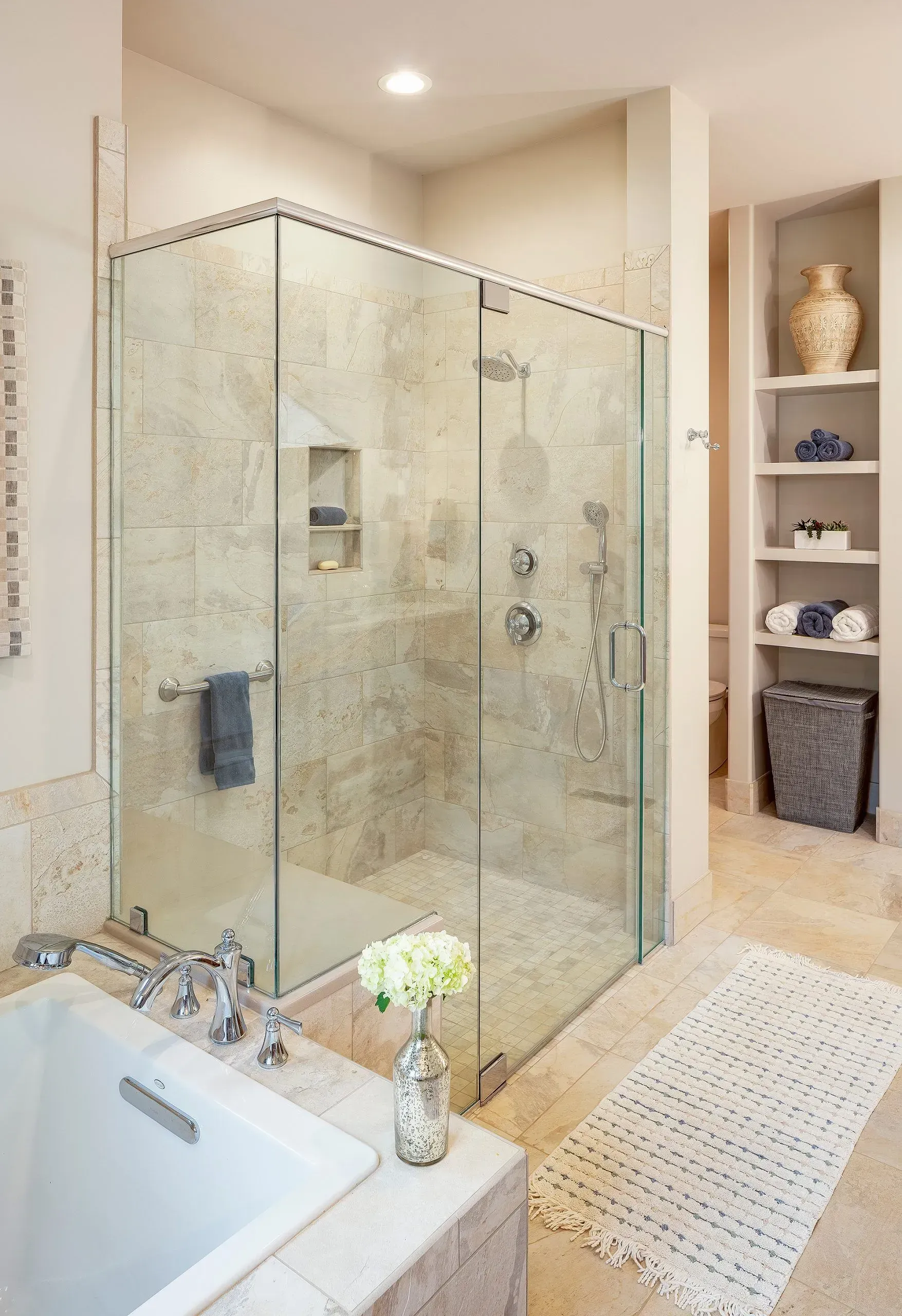 A luxurious bathroom features a glass shower, soaking tub, and built-in shelves with towels.