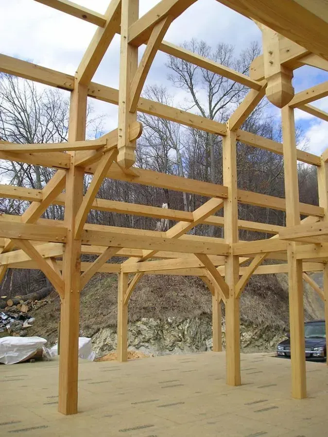 Wooden timber frame under construction with arches, beams, and support posts in a natural setting.