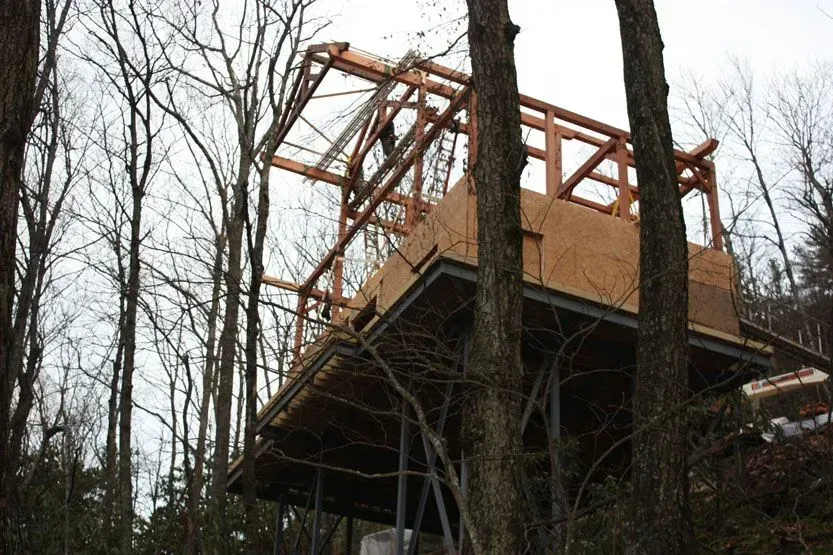 A wooden structure under construction in a wooded area, supported by metal beams.