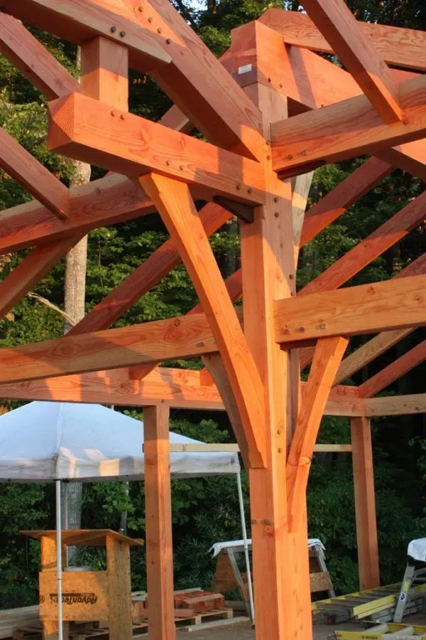 Wooden timber frame construction, exposed joinery, beams and supports, outdoor setting with light tent.