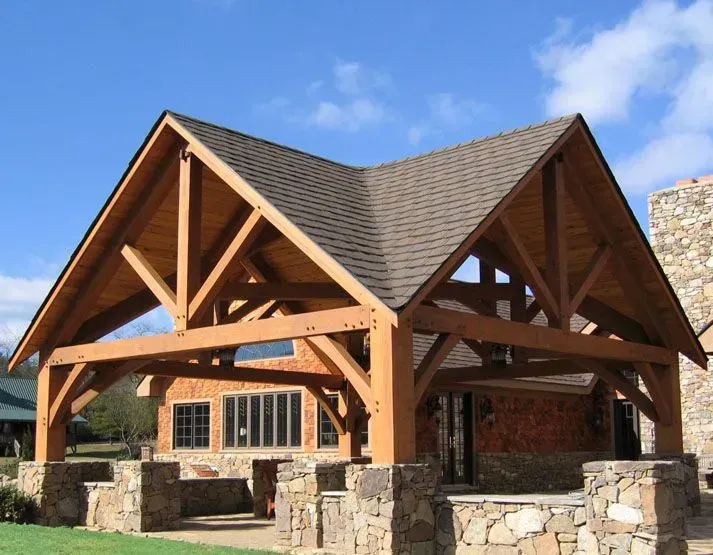 Wooden pavilion with brown roof and rock walls, set against a blue sky.