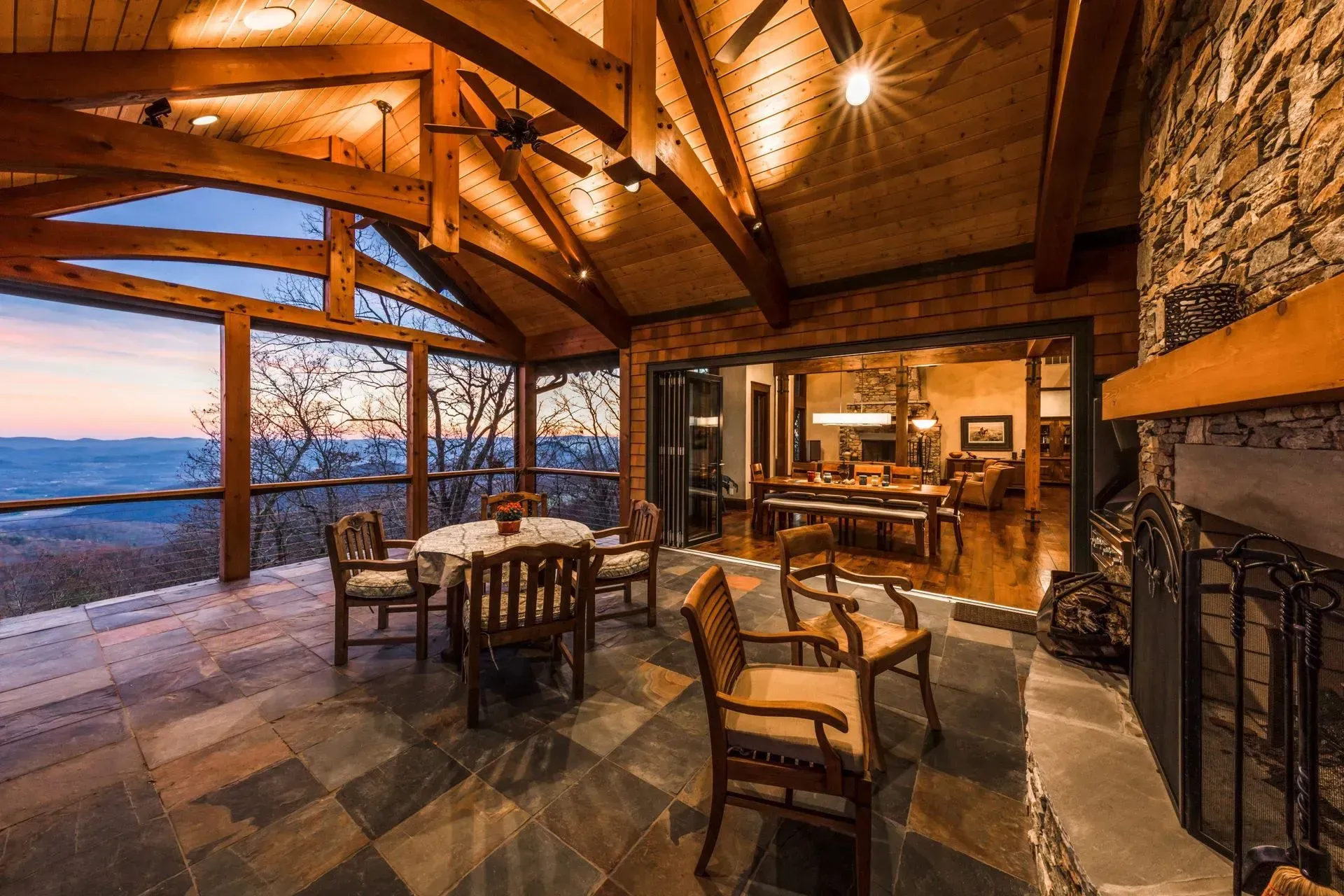 Screened porch with dining set, stone fireplace, and open sliding doors to interior. Mountain view at sunset.