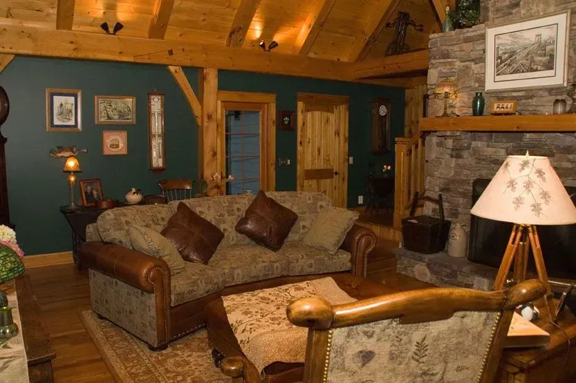 Cozy living room with stone fireplace, wooden beams, green walls, and brown leather furniture.
