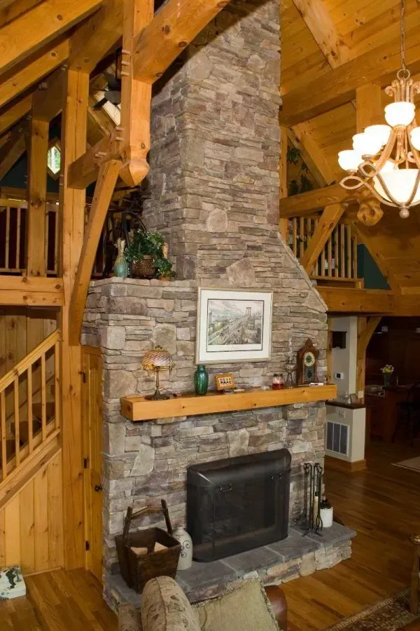 Stone fireplace in a wood-paneled room, framed by exposed wooden beams and a staircase.