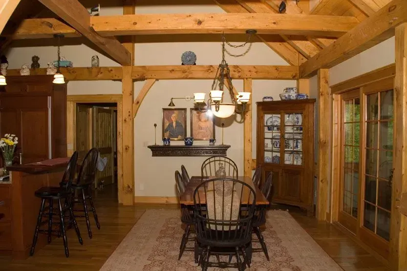 Dining room with wooden beams, table, chairs, cabinet, and bar with stools.