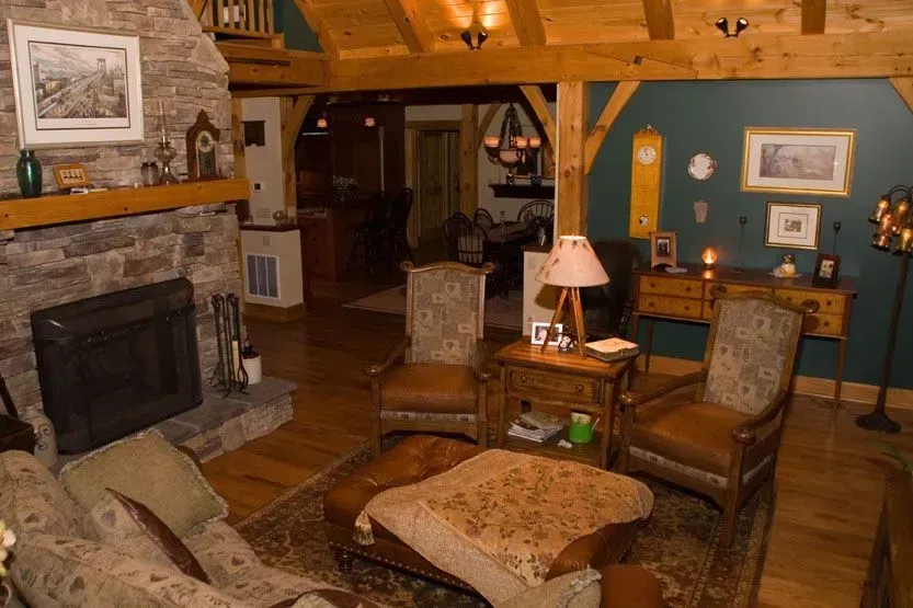 Cozy living room with stone fireplace, wood beams, armchairs, and dark green walls.