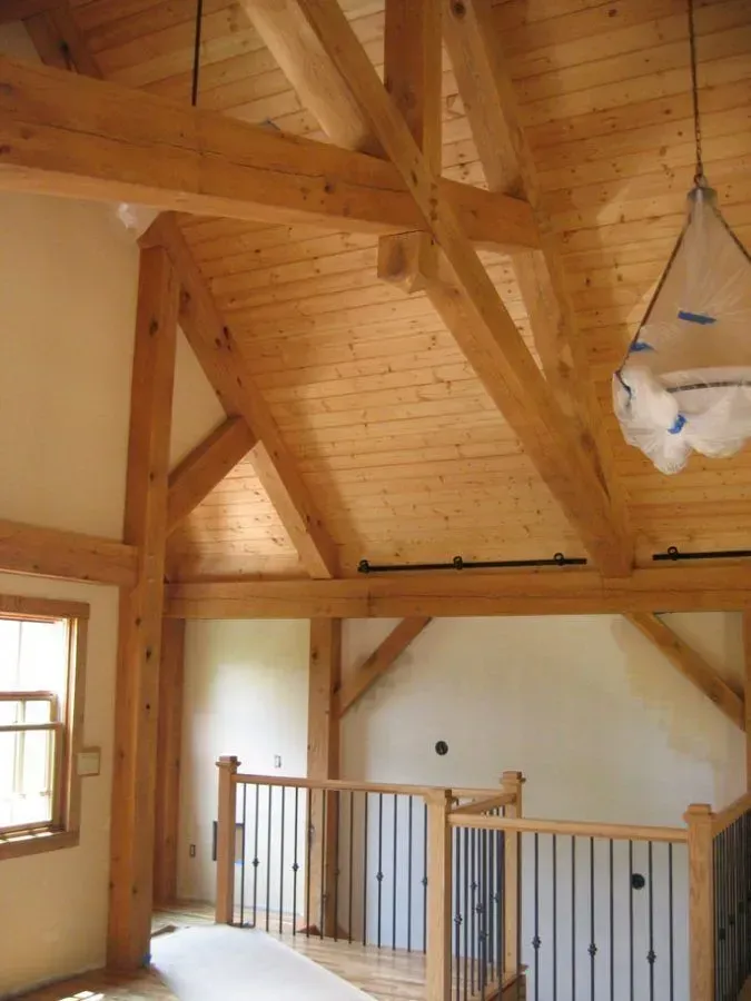 Interior view of a timber-framed building with a second-floor railing. Wooden beams and a light wood ceiling.