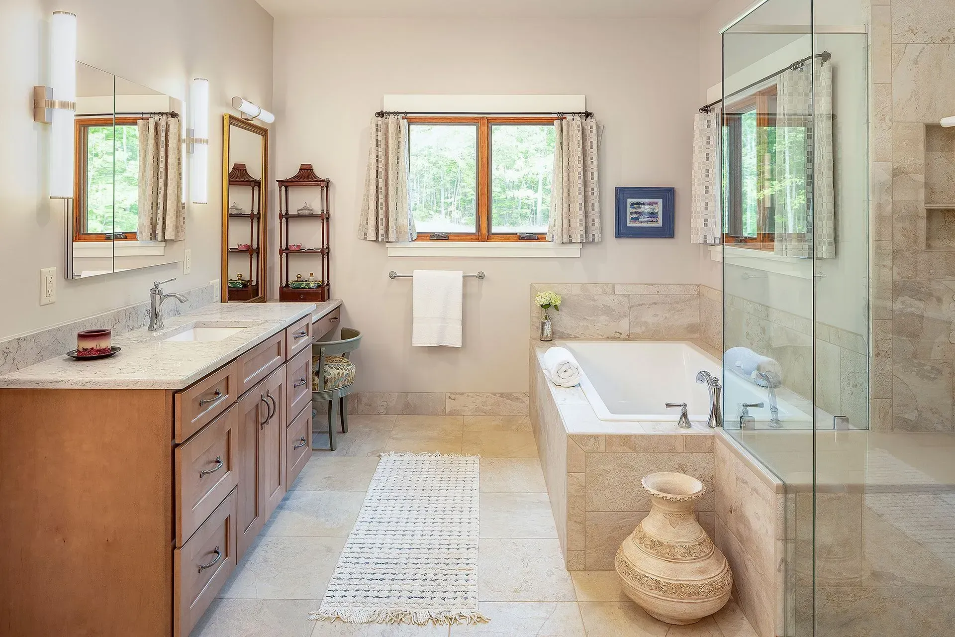 Bathroom with a vanity, bathtub, shower, and window. Beige tile, wood accents, and neutral color scheme.