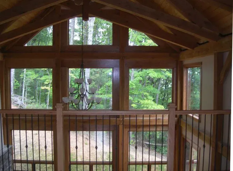 Interior view of a wooden framed room with large windows overlooking a forest. A chandelier hangs in the center.