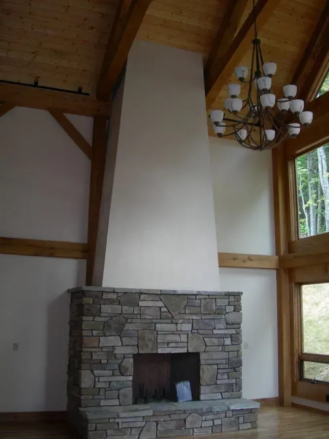 Stone fireplace with light beige walls and wooden beams, chandelier hangs above.