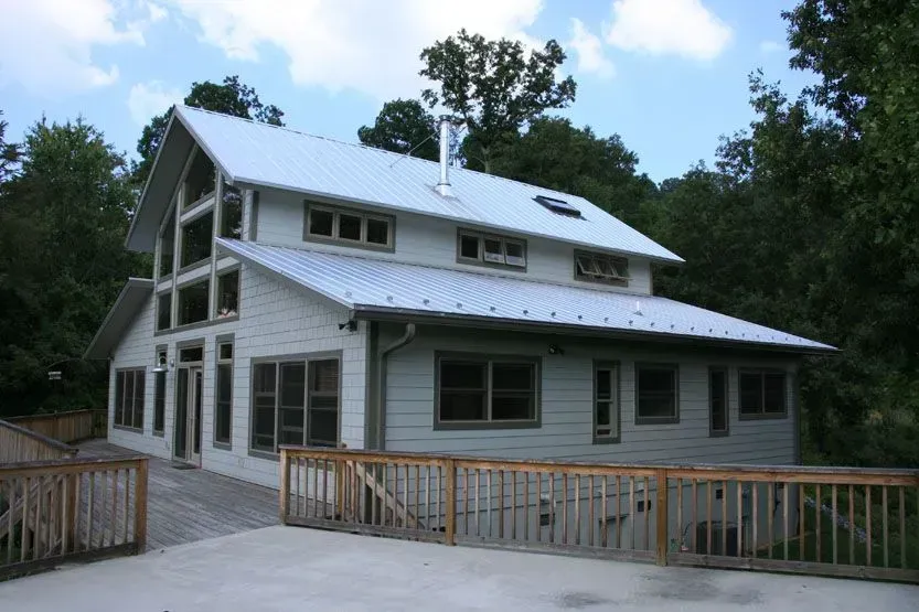 White two-story house with a metal roof surrounded by trees and a wooden deck.