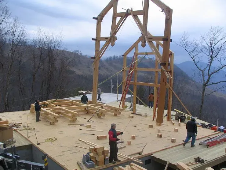 Construction site with wooden frame being erected on a flat platform overlooking a mountainous landscape.