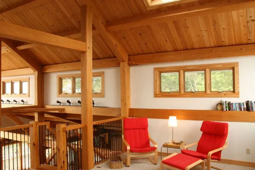 Wooden-beamed interior with red chairs, windows, and a loft.