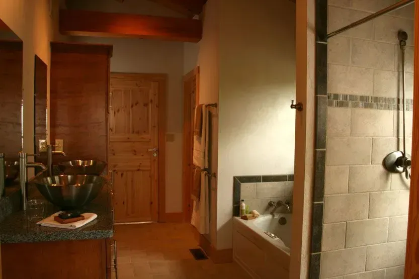 Bathroom with wood cabinets, stone-tiled shower, and a bathtub. Soft lighting.