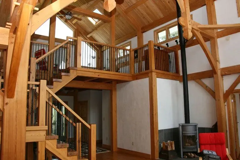 Wooden interior with a loft, staircase, fireplace, and red chair.
