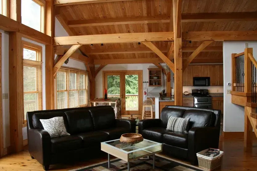 Living room with wood beams, leather sofas, glass coffee table, and open to the kitchen and outdoors.