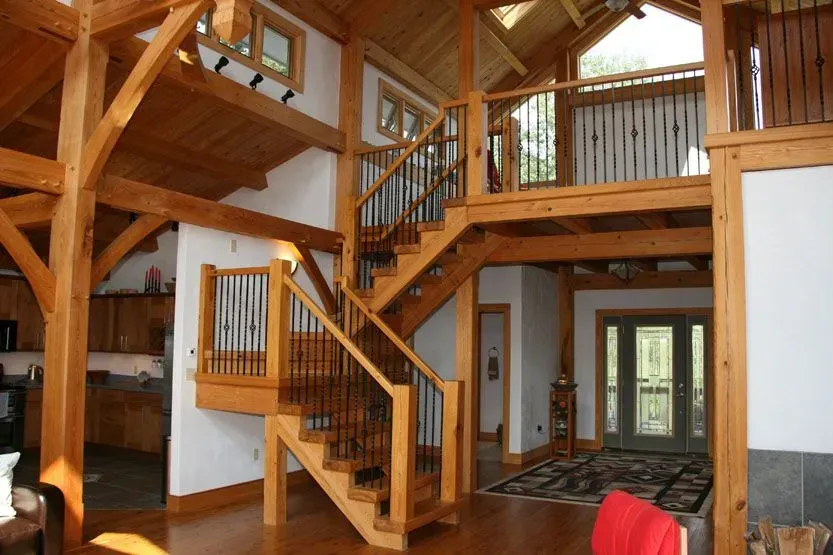 Wooden interior with a staircase, second-floor landing, and tall, beamed ceilings.