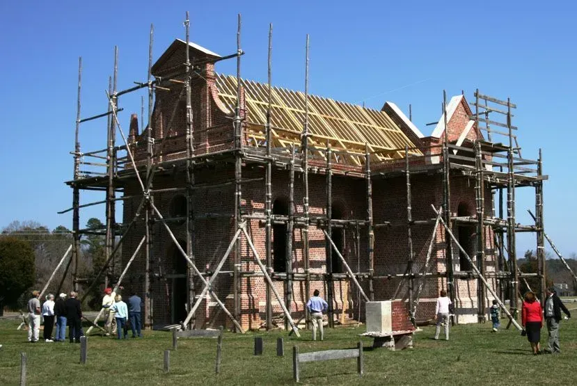 Building under construction, red brick, wood scaffolding, people observing outdoors.