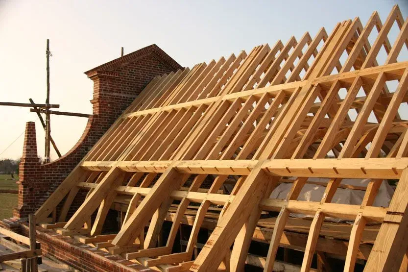 Wooden roof framing under construction with a brick chimney in the background.
