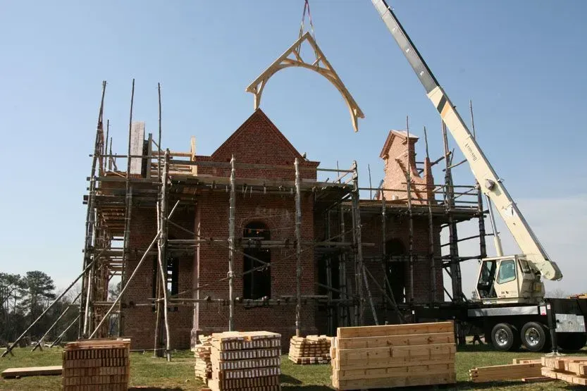 Construction of a brick building; crane lifting a wooden architectural feature.