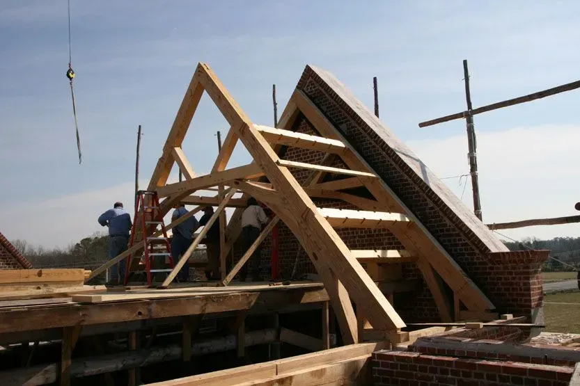 Construction of a wooden roof frame on a building, with workers and a crane against a blue sky.