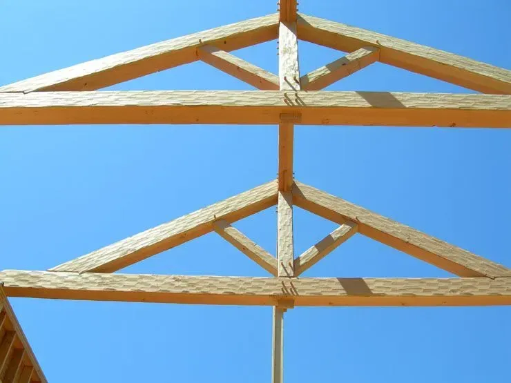Wooden roof trusses against a bright blue sky.