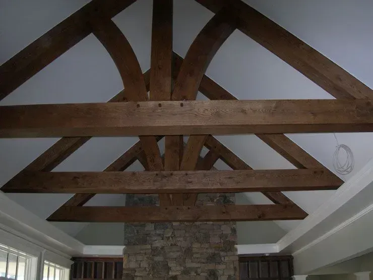 Wooden ceiling beams in a room with stone fireplace and white walls.