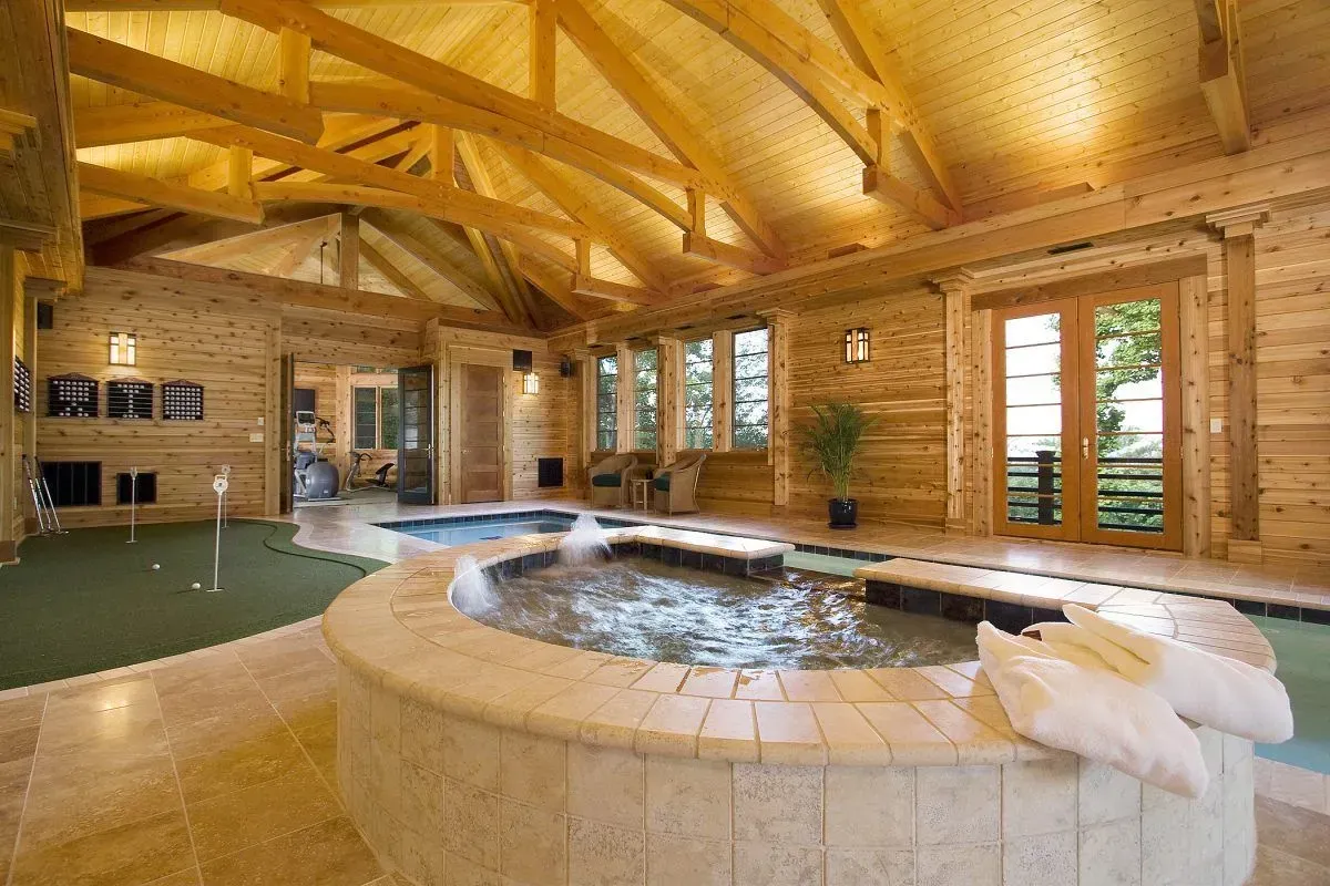 Luxury indoor spa with hot tub, putting green, and wooden beams.