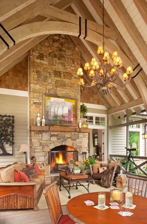 Rustic porch with stone fireplace, wood beams, warm colors, and a chandelier.