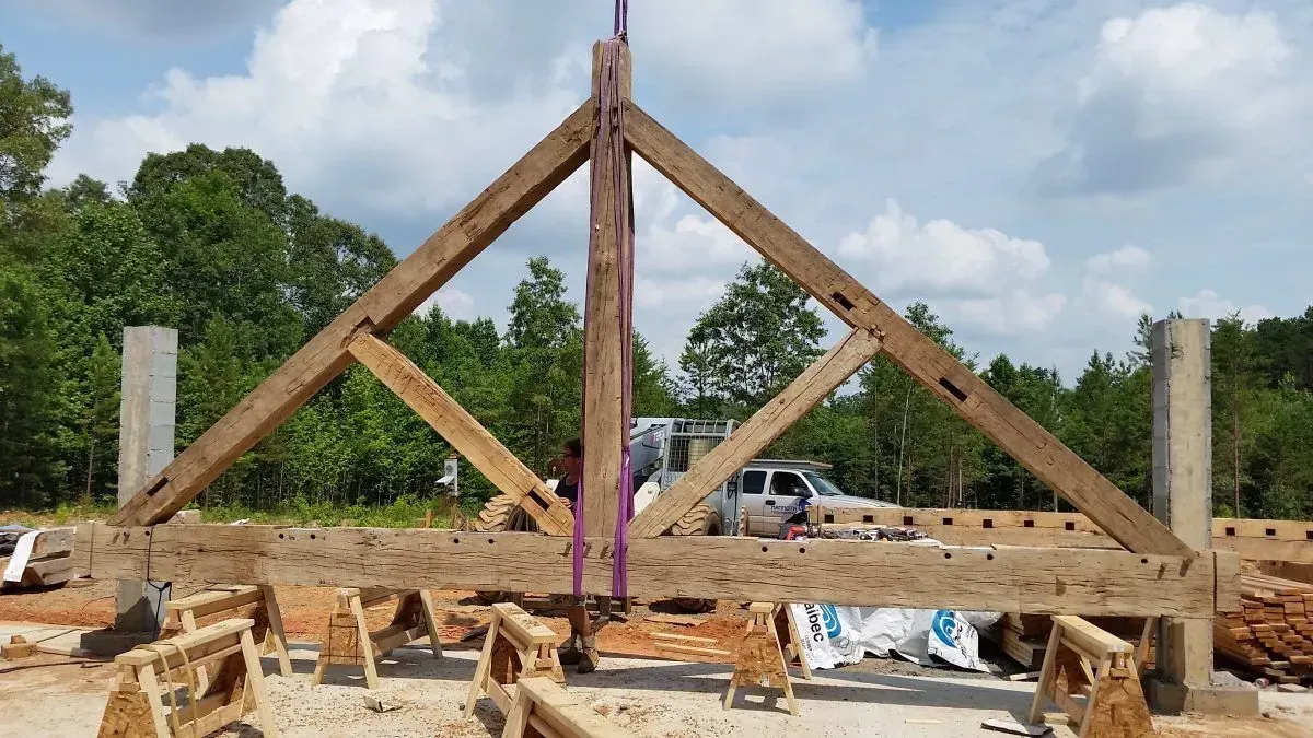 A timber-framed roof truss being lifted into place on concrete columns at a construction site.