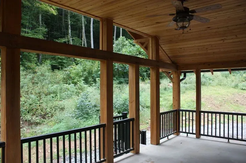 Wooden porch with black railings overlooking a green forest.