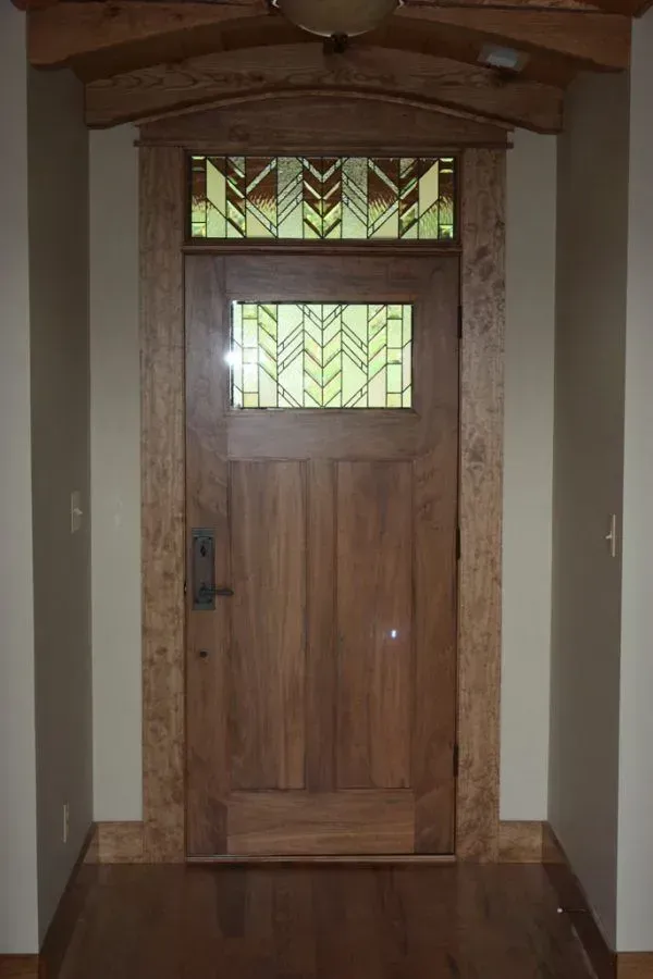 Wooden Craftsman-style door with stained glass transom and sidelights, brown trim, and interior hallway.