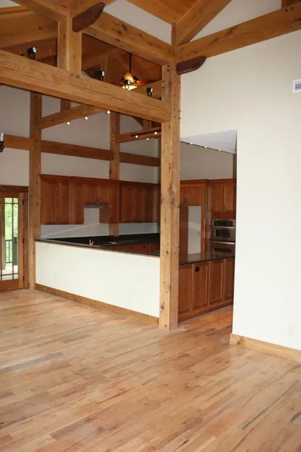 Spacious room with wood beams and flooring, kitchen in the background.