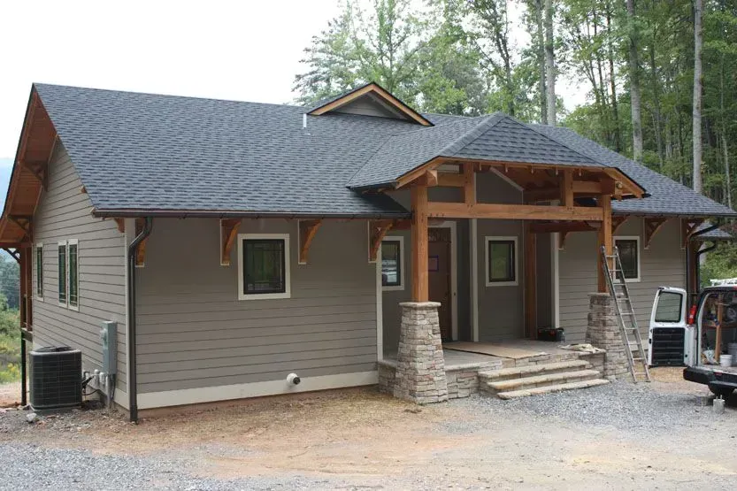 Tan house with brown trim and stone columns, surrounded by trees.
