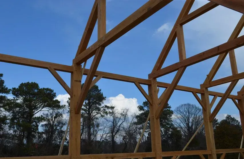 Wooden timber frame of a building under construction, against a blue sky with clouds.