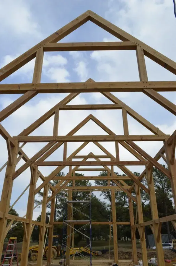 Wooden frame of a building under construction, with a gabled roof against a cloudy sky.