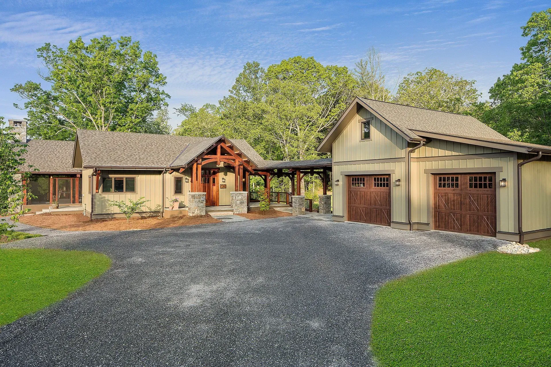 Beige Craftsman home with a gravel driveway, garage, and lush green lawn.