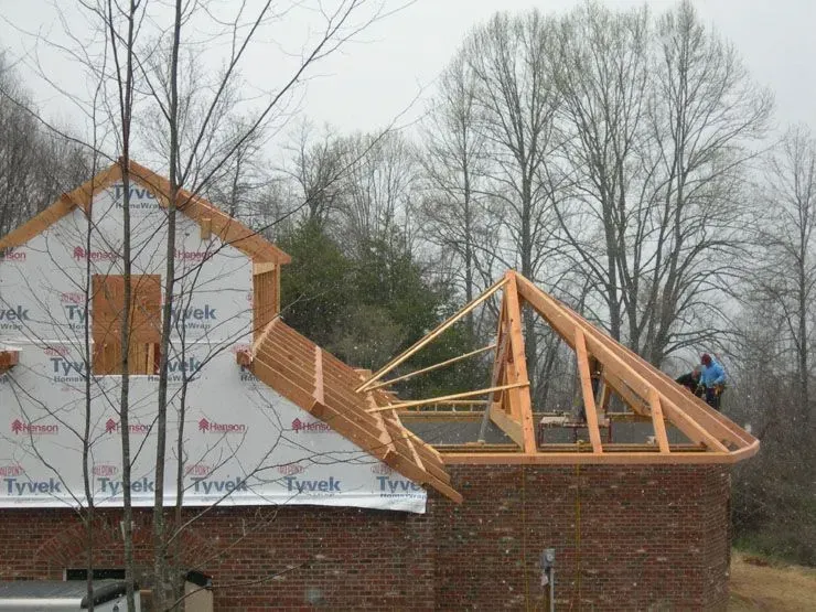 Construction site: framing new roof with worker on the structure, bricks, and Tyvek-covered wall.