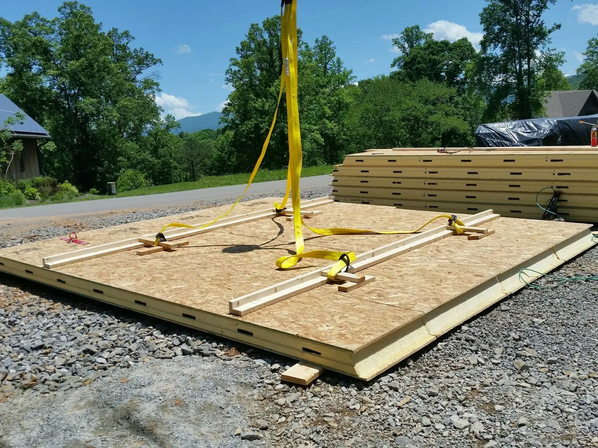 A large wall panel being lifted by a crane on a construction site. Yellow straps secure it.