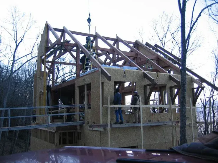 Construction of a wooden building: workers installing roof trusses. Exterior view; daylight.