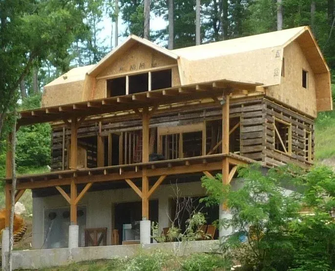 House under construction on a hillside; wood frame, exposed beams, unfinished siding, porch.
