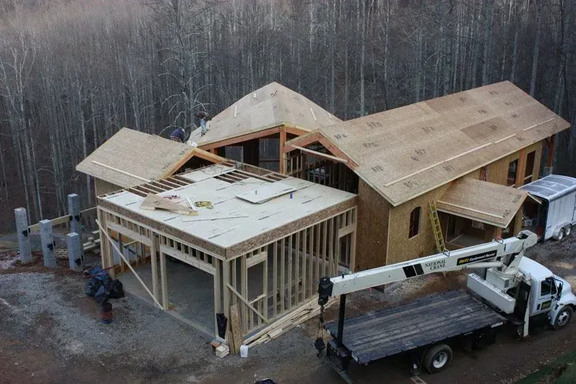 House under construction with crane, framing, plywood roof. Exterior setting, natural light.